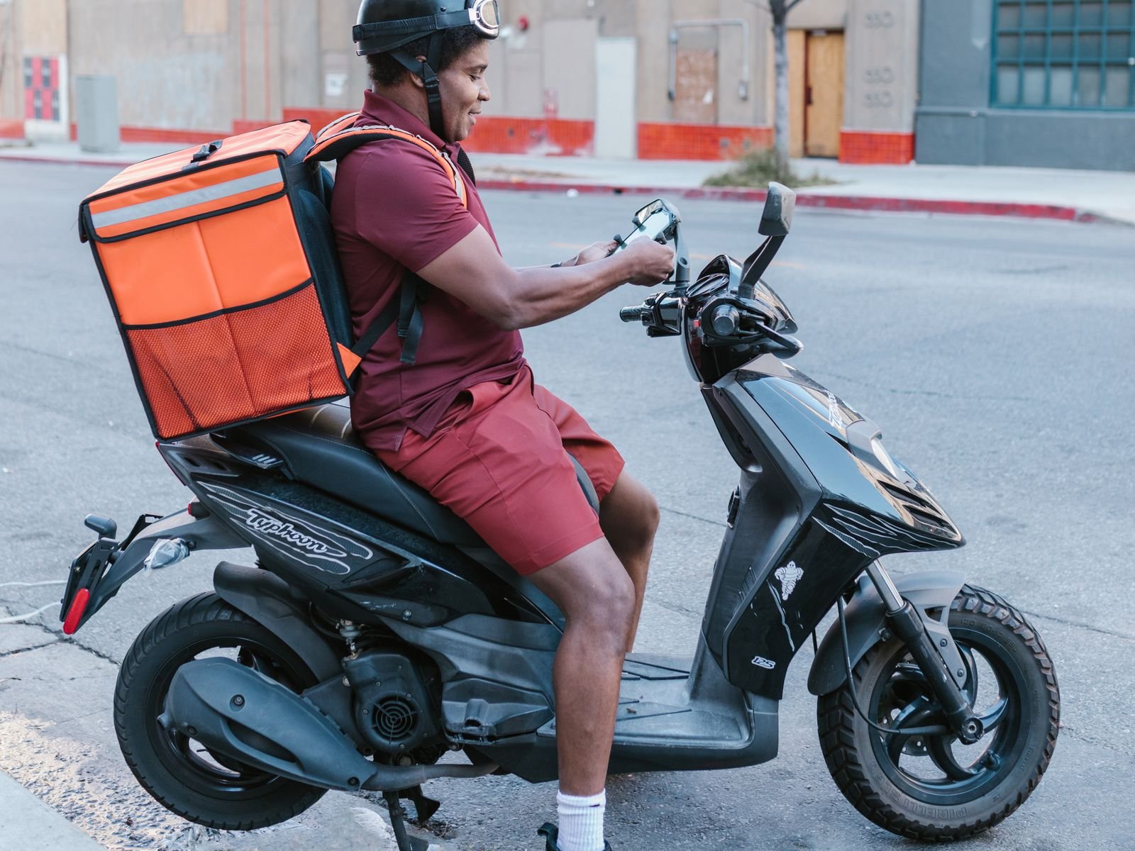 Διανομέας σε σκούτερ ελέγχει παραγγελία delivery στο κινητό
